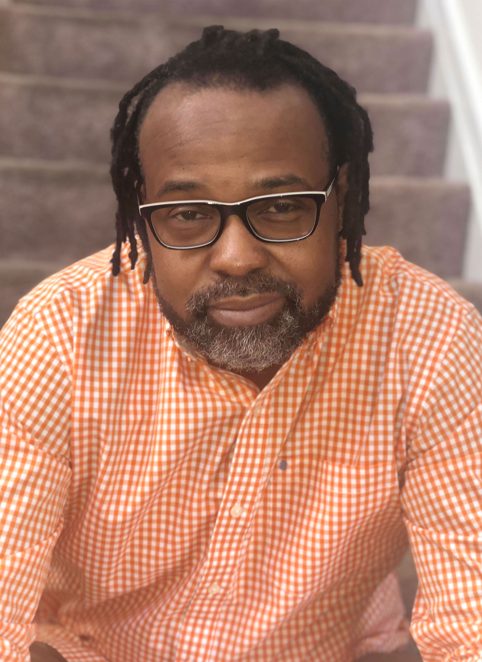 A man with dreads and glasses sitting on steps.