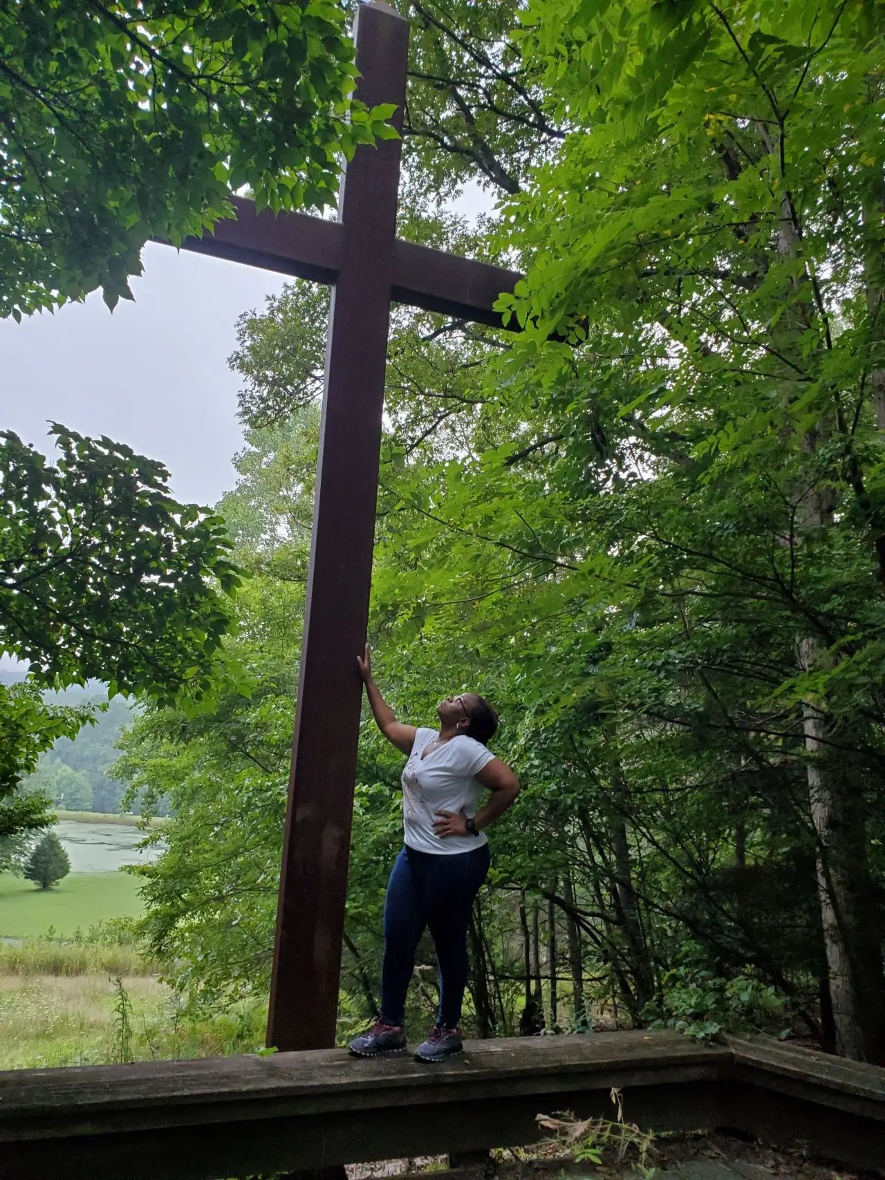 A woman standing next to a cross in the woods.